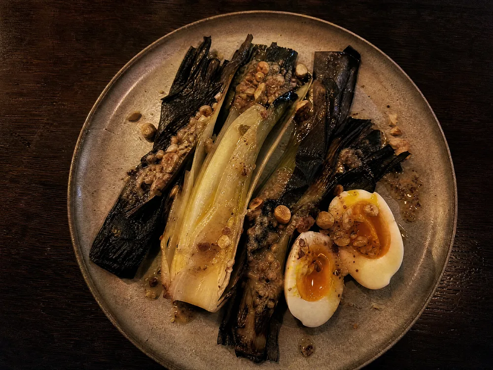 Poireaux brûlés ouverts sur une assiette, œuf mollet et vinaigrette