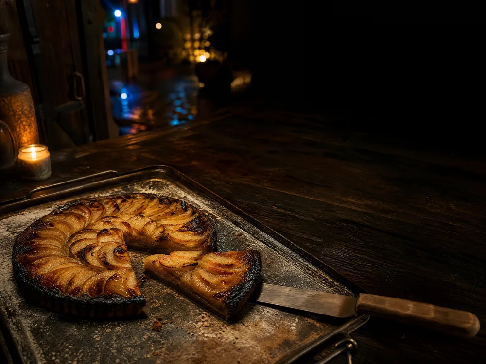 Tarte aux pommes sortie du four à bois, bords caramélisés, une part levée